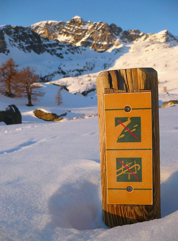 Panneau de pictogrammes de "réglementation" devant le mont Bégo en hiver